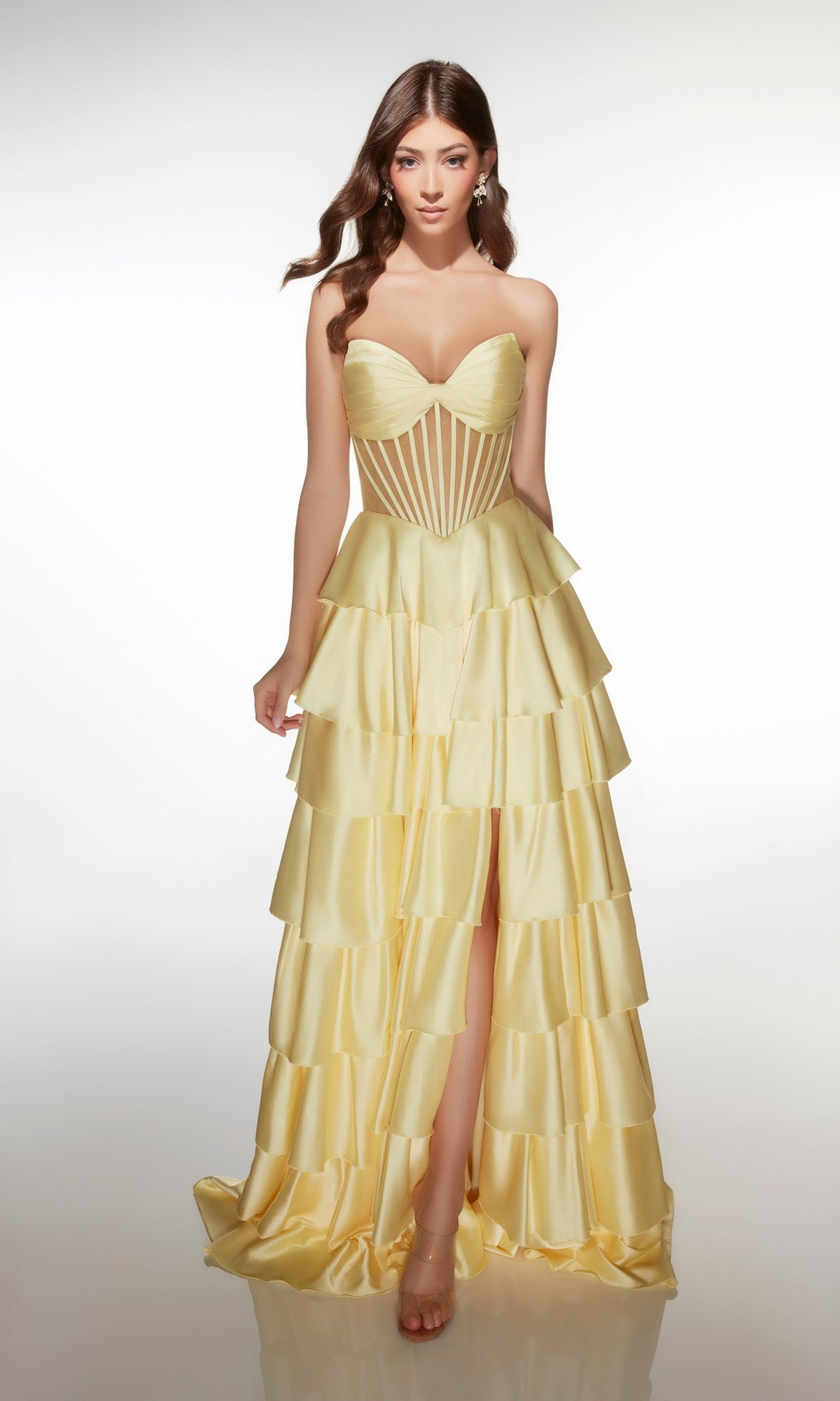 A woman stands against a plain white background wearing the light yellow Alyce 62056 long prom dress, featuring a strapless satin design with a sweetheart neckline and a tiered ruffle A-line skirt.